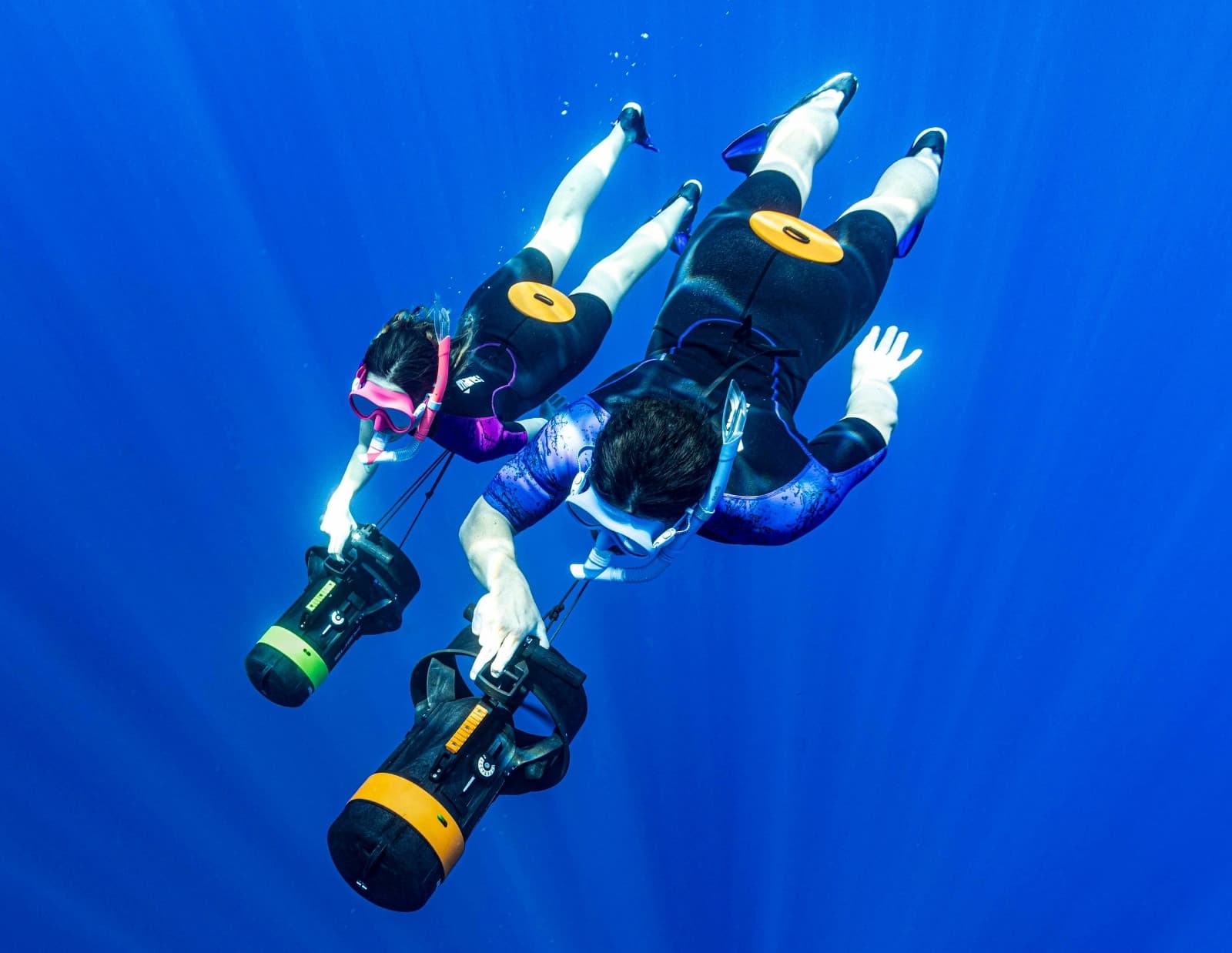Due subacquei in apnea scendono in acqua blu impugnando un DPV SUEX compatto